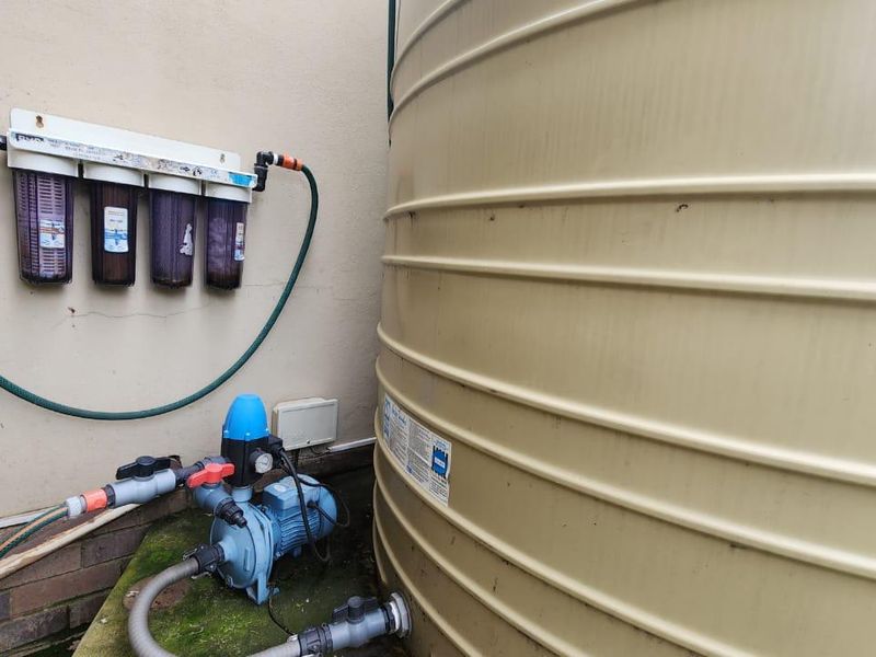 Exterior utility area featuring a large water storage tank, integrated water pump, and a multi-stage water filtration system mounted to the wall.