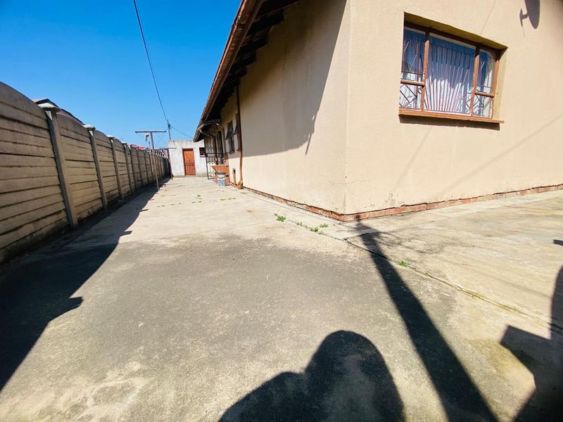 A view of the rear exterior area featuring a concrete paved pathway, precast boundary wall, and the side elevation of the house with security bars.