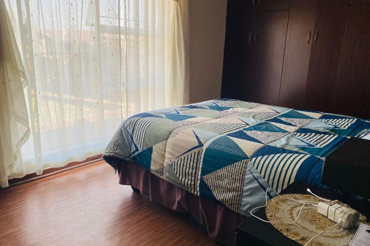A bedroom featuring laminate flooring, built-in dark wood cupboards, and a sliding glass door providing natural light.