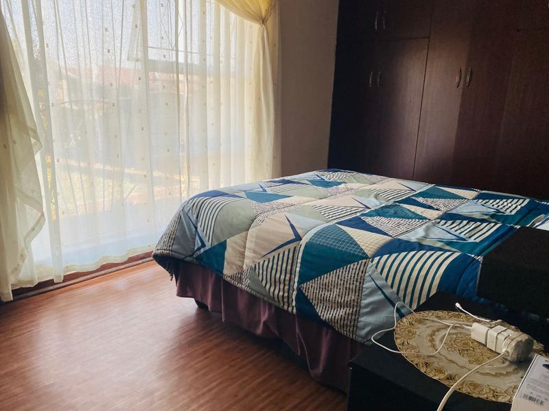 A bedroom featuring laminate flooring, built-in dark wood cupboards, and a sliding glass door providing natural light.