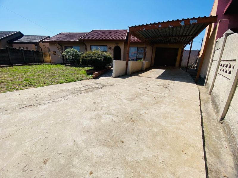 Front exterior view of the house featuring a concrete driveway, a carport, and a small front garden area.