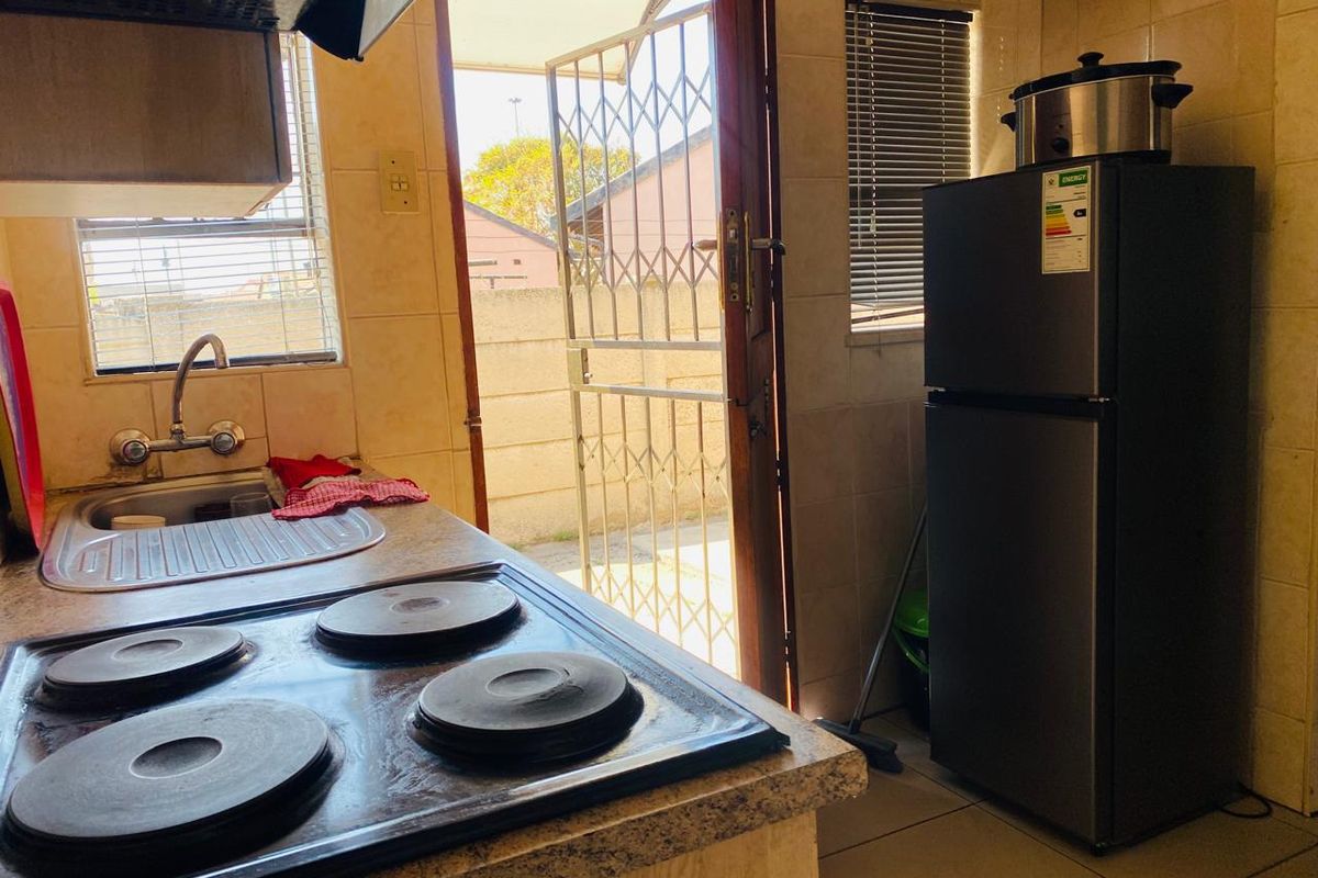Functional kitchen featuring a built-in electric hob, extractor fan, stainless steel sink, and direct access to the exterior via a security gate.
