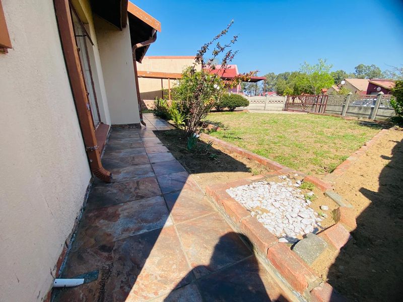 Rear exterior view featuring a tiled patio area, brick-edged garden beds, and a precast concrete boundary wall.