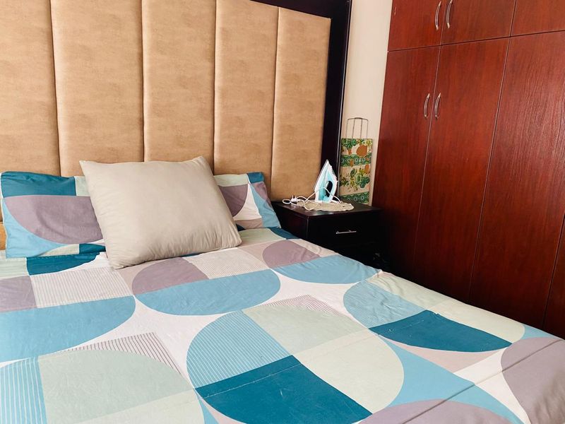 A bedroom featuring a large upholstered headboard and a full-height built-in wooden wardrobe.