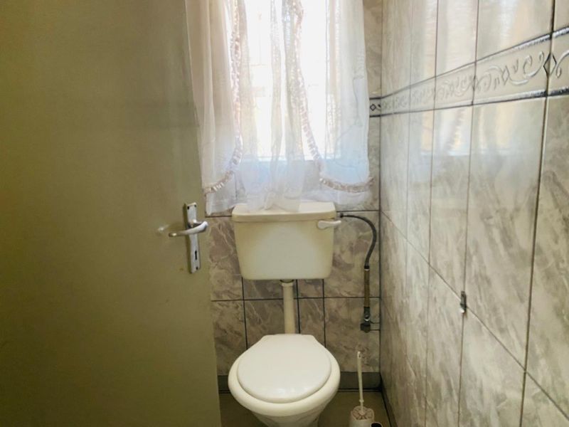 A compact bathroom featuring tiled walls and a standard toilet, requiring minor maintenance and cosmetic updates to improve its overall condition.