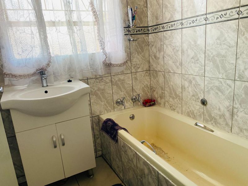 A functional bathroom featuring a vanity cabinet with basin and a bathtub with wall-to-wall tiling.