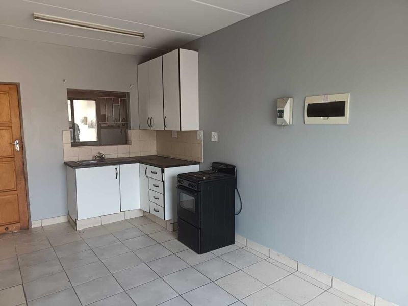 A compact, functional kitchen featuring basic white cabinetry, a stainless steel sink, tiled flooring, and a freestanding stove in an open-plan layout.