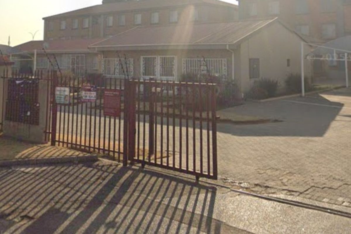 Front exterior view of the apartment complex featuring a gated entrance, paved driveway, and security fencing.