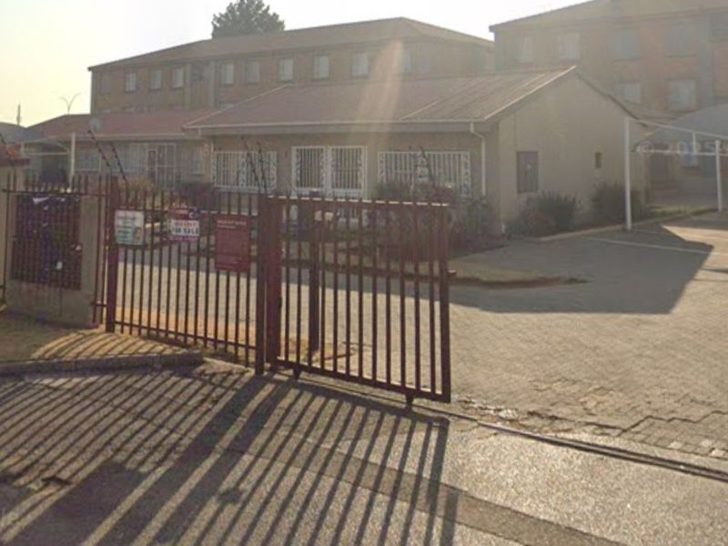 Front exterior view of the apartment complex featuring a gated entrance, paved driveway, and security fencing.