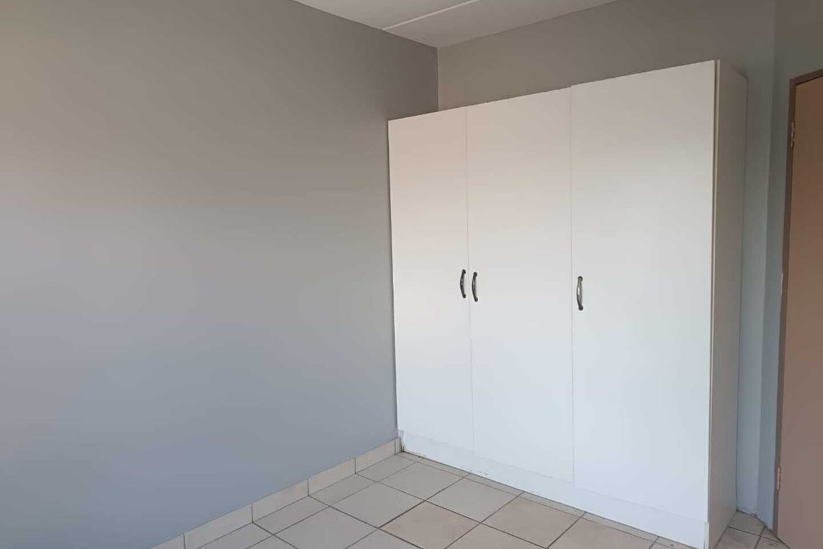 A simple bedroom featuring neutral grey walls, tiled flooring, and a white built-in wardrobe.