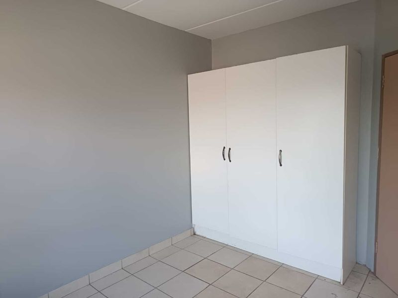 A simple bedroom featuring neutral grey walls, tiled flooring, and a white built-in wardrobe.