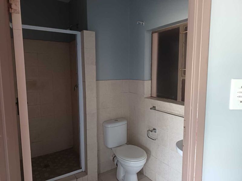 A functional bathroom featuring a shower enclosure, toilet, and washbasin with neutral wall tiling and a window for natural light.