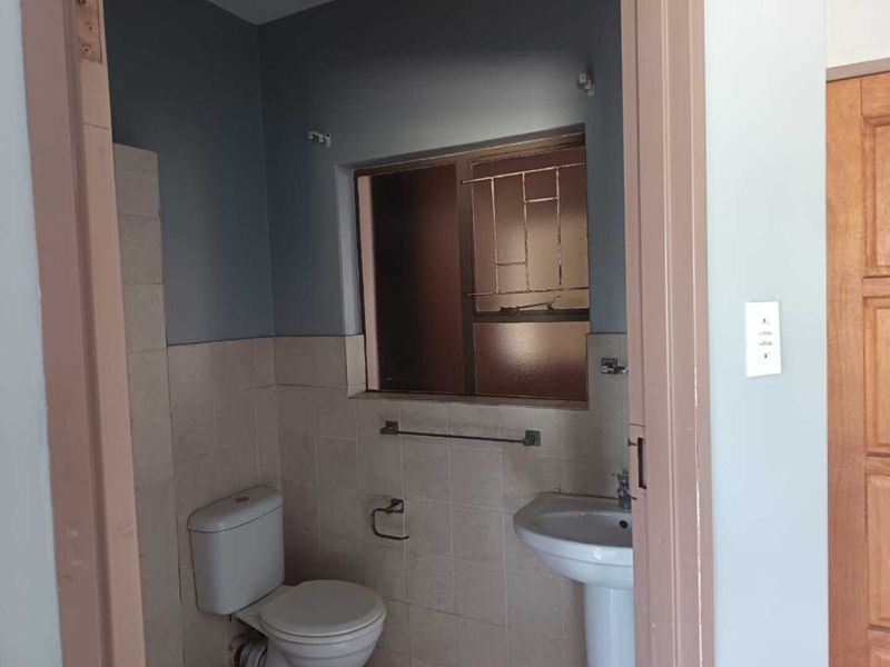 A compact bathroom featuring a pedestal basin, toilet, and tiled walls, currently in need of cosmetic updates and maintenance.