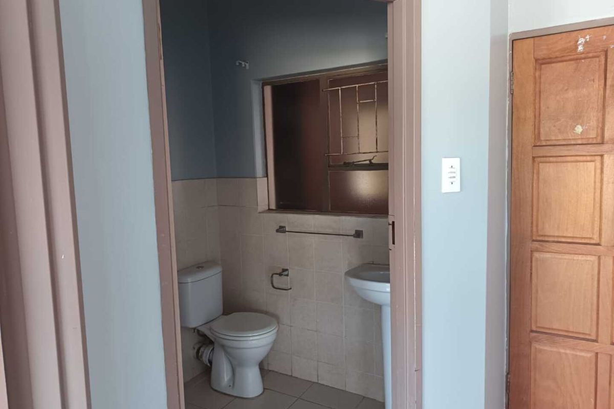 A compact, empty bathroom featuring a pedestal washbasin, toilet, and tiled finishes, requiring cosmetic updates to modernize the space.