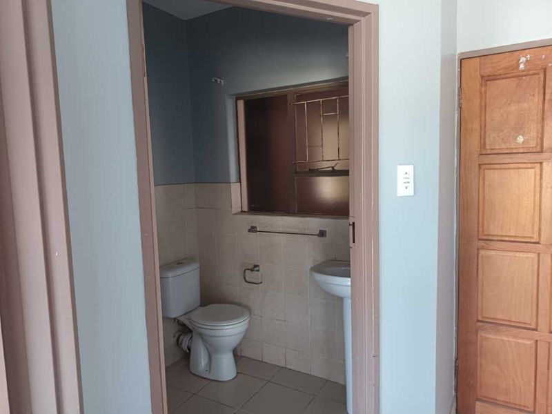 A compact, empty bathroom featuring a pedestal washbasin, toilet, and tiled finishes, requiring cosmetic updates to modernize the space.