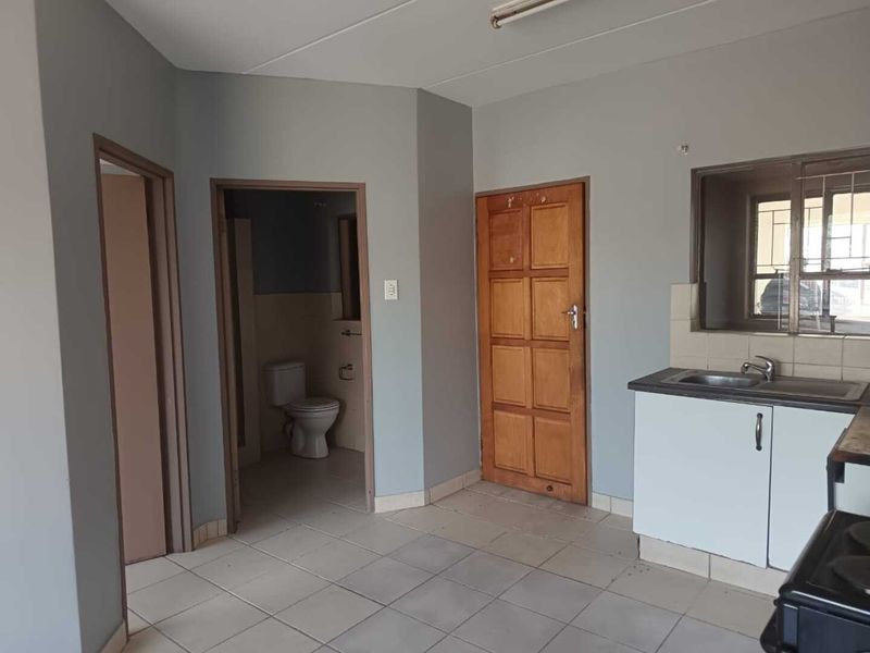 Open plan living area featuring tiled flooring, basic kitchen cabinetry with sink, and access to an adjacent bathroom.