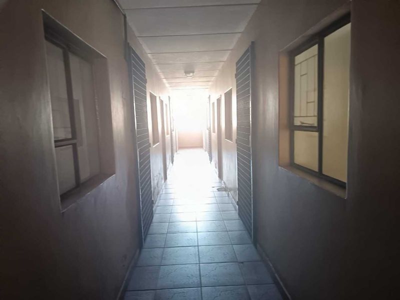 A narrow apartment hallway featuring tiled flooring and multiple security gates leading to individual units.