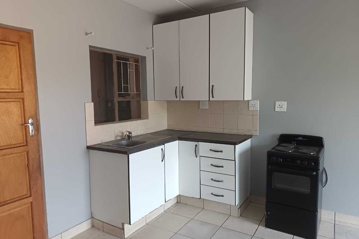 A functional kitchen featuring white cabinetry, laminate countertops, a stainless steel sink, tiled backsplash, and ceramic floor tiles.