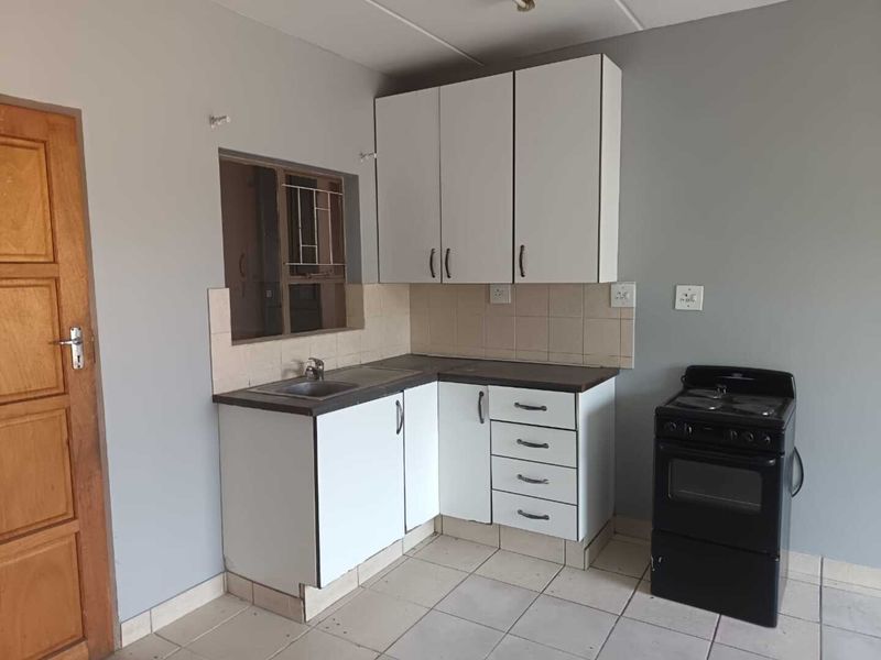 A functional kitchen featuring white cabinetry, laminate countertops, a stainless steel sink, tiled backsplash, and ceramic floor tiles.
