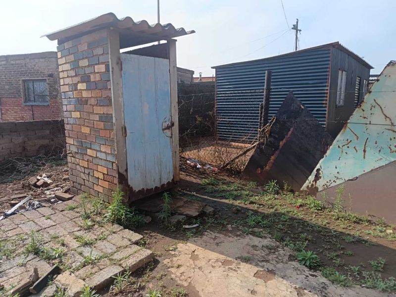 Rear yard area featuring a brick outbuilding, a corrugated metal shed, and perimeter fencing in need of significant maintenance and repair.
