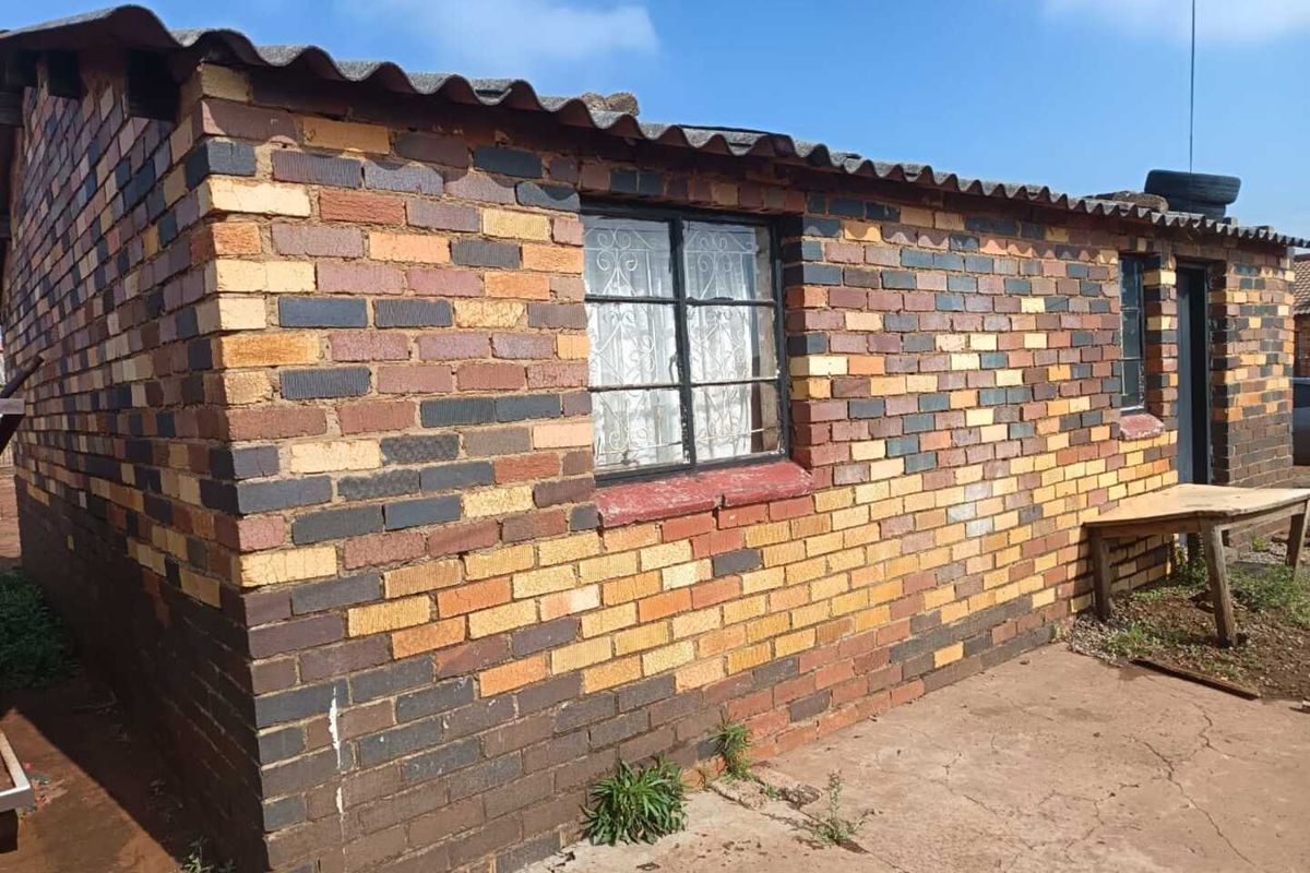 Exterior view of a face brick house featuring corrugated roof sheeting and security-barred windows, set on a concrete apron.