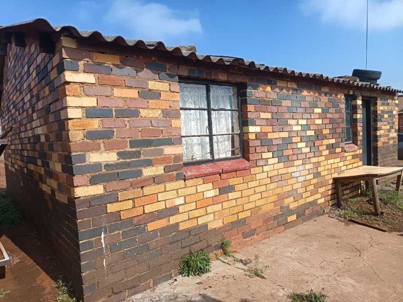 Exterior view of a face brick house featuring corrugated roof sheeting and security-barred windows, set on a concrete apron.