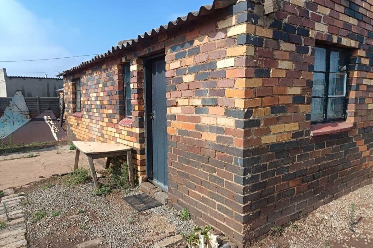 Exterior view of a face brick structure featuring corrugated roof sheeting and steel frame windows, showing signs of age and weathering.
