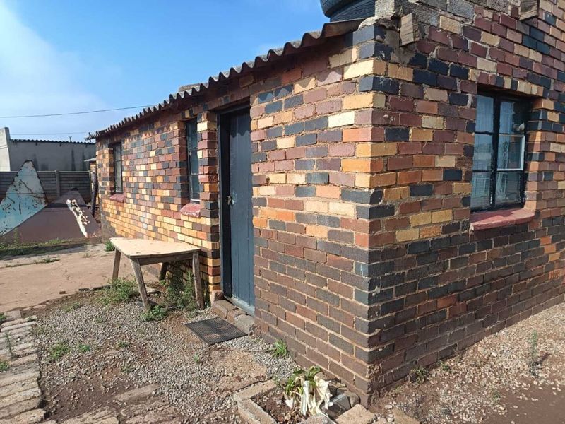 Exterior view of a face brick structure featuring corrugated roof sheeting and steel frame windows, showing signs of age and weathering.
