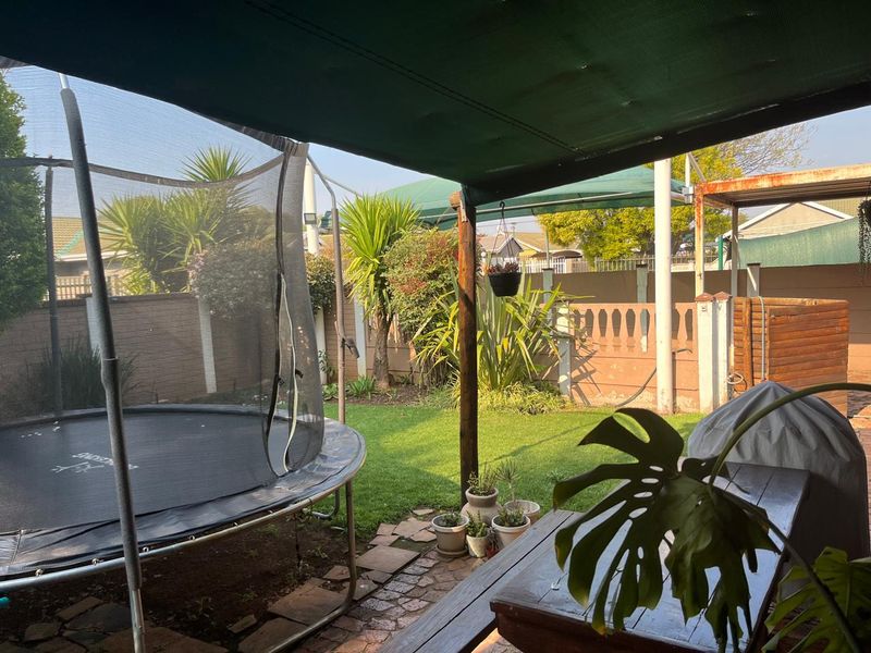 A covered outdoor patio area featuring brick paving and timber support posts, overlooking a private garden with boundary walling.