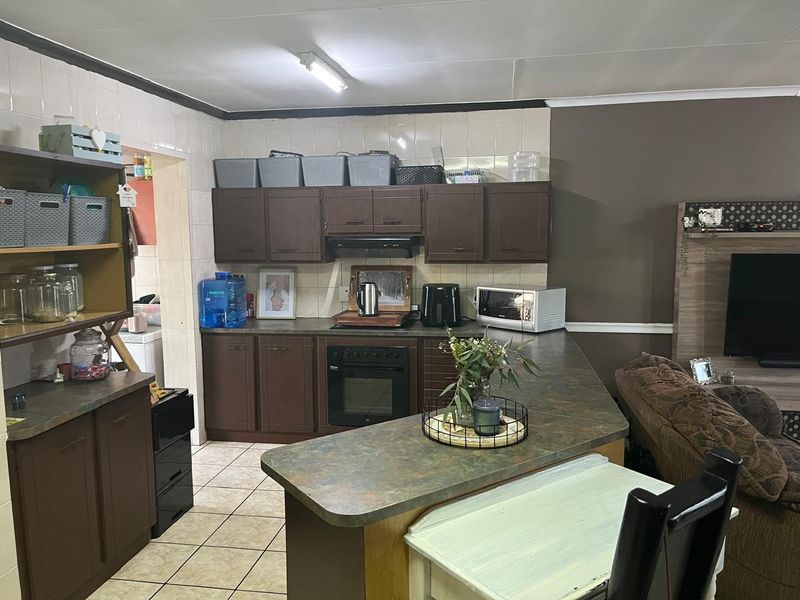 Open plan kitchen featuring dark wood cabinetry, laminate countertops, built-in oven, and tiled flooring, seamlessly connecting to the adjacent living area.