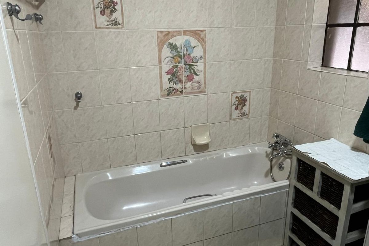 A dated bathroom featuring a built-in bathtub with tiled surround and decorative wall accents, requiring cosmetic updates to modernize the space.