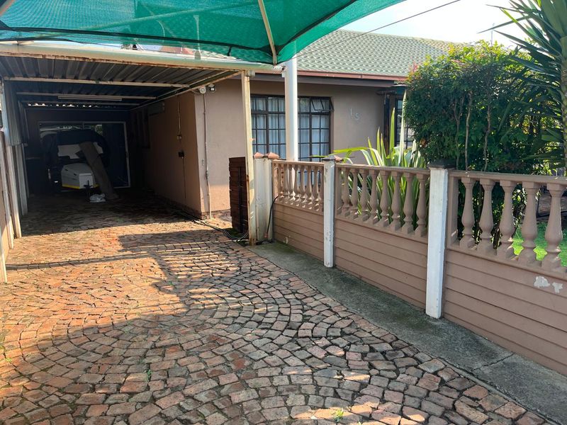 Front exterior view featuring a cobblestone driveway, covered carport with shade cloth, and a decorative precast concrete boundary wall.