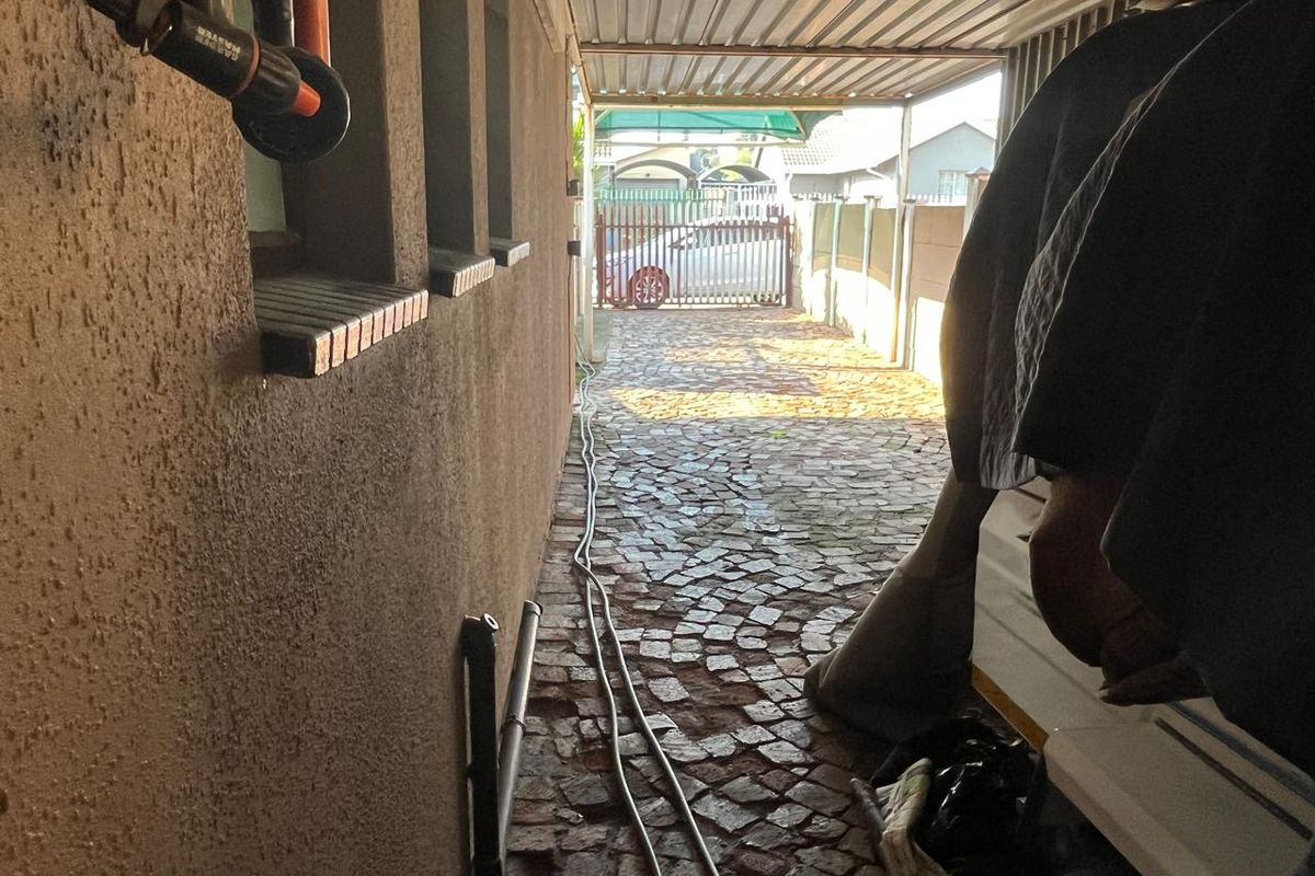 A narrow paved side passage featuring a metal carport structure, boundary wall, and secure gated access to the driveway.