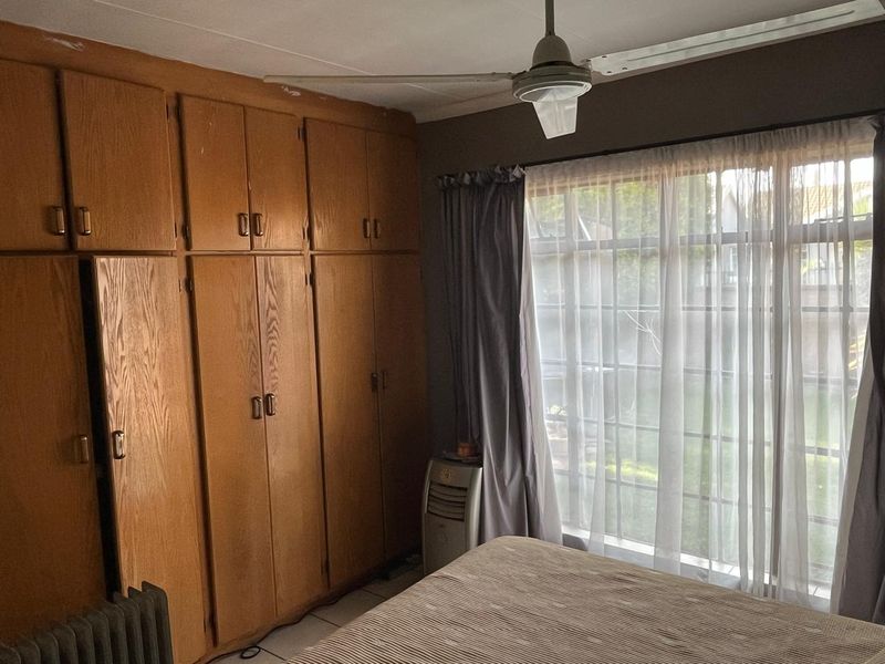 Bedroom featuring extensive built-in wooden cabinetry, a ceiling fan, and a large window providing natural light.