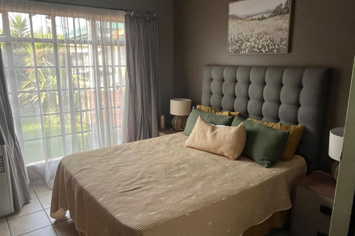 A comfortable bedroom featuring tiled flooring, a ceiling fan, and a large sliding glass door providing access to the outdoor area.