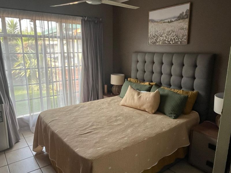 A comfortable bedroom featuring tiled flooring, a ceiling fan, and a large sliding glass door providing access to the outdoor area.