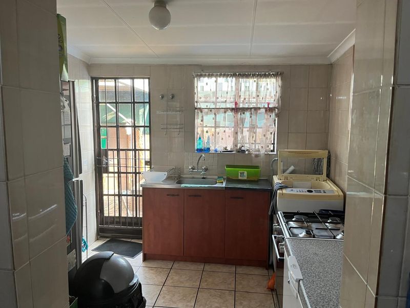Functional scullery area featuring built-in cabinetry, a stainless steel sink, gas hob, and direct access to the exterior via a security gate.