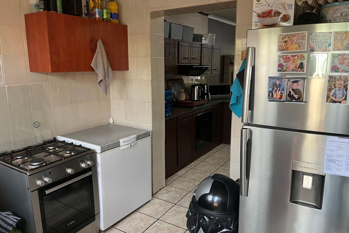 A functional kitchen area featuring tiled walls and flooring, built-in cabinetry, and a gas stove, with an adjacent scullery or prep area visible.