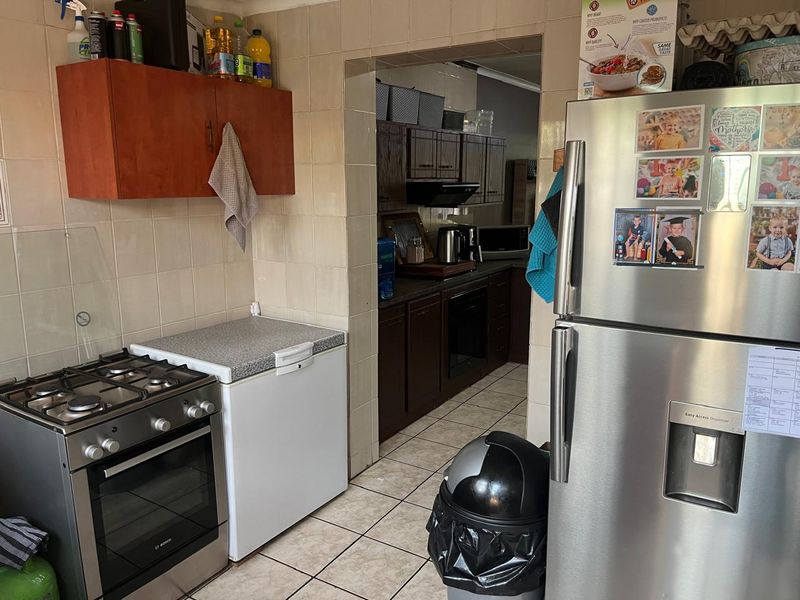 A functional kitchen area featuring tiled walls and flooring, built-in cabinetry, and a gas stove, with an adjacent scullery or prep area visible.