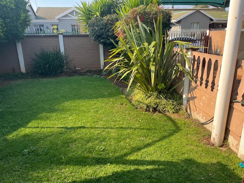 A private rear garden featuring a well-maintained lawn, established landscaping, and secure brick boundary walls with decorative concrete balustrades.