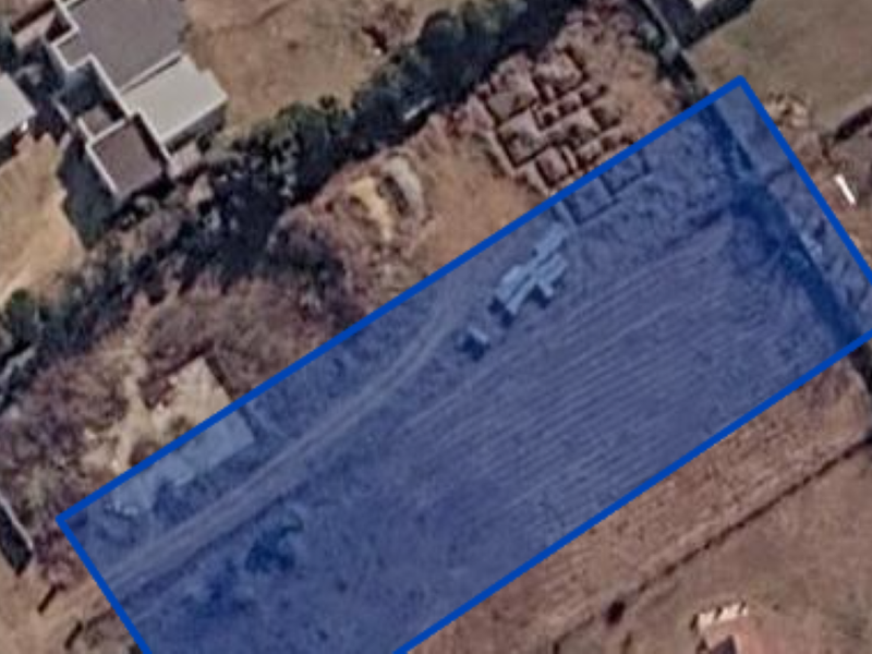 An aerial view of a vacant residential plot with a blue boundary overlay indicating the property lines.