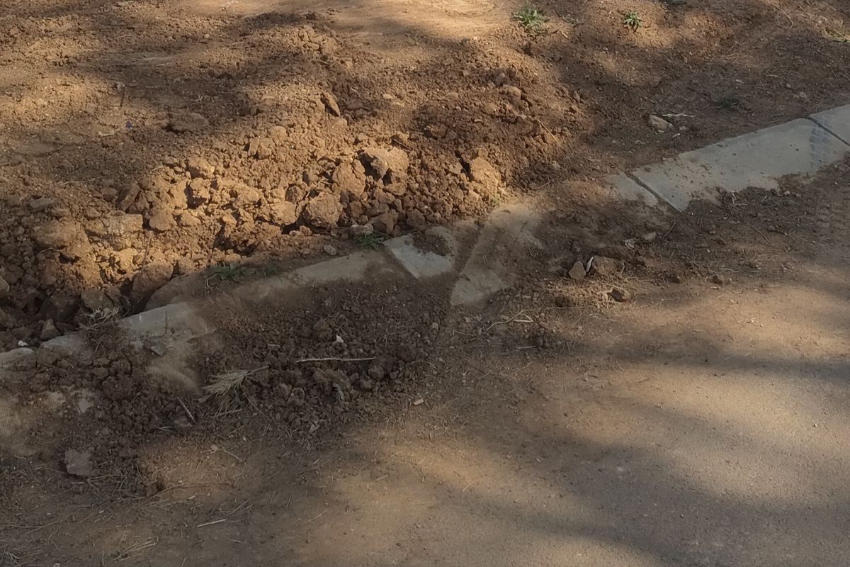 A view of the vacant residential plot showing the street-side concrete kerbing and the rear boundary wall.