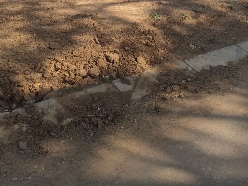 A view of the vacant residential plot showing the street-side concrete kerbing and the rear boundary wall.