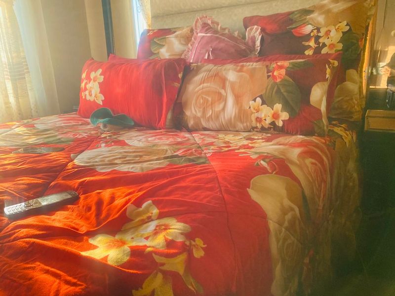 A bedroom interior featuring a bed with floral bedding, illuminated by natural light from a nearby window.