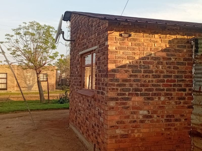 Rear view of the property featuring exposed brickwork, a corrugated metal extension, and a roof-mounted solar water heater.