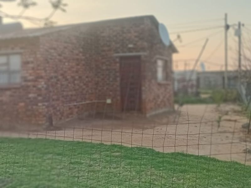 A view of the rear exterior of a face brick house featuring a simple yard and wire mesh perimeter fencing.
