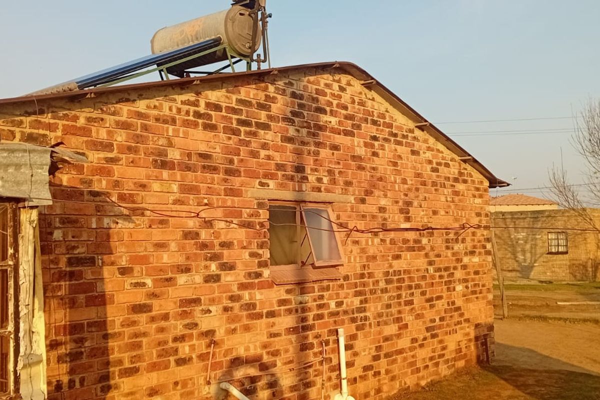 Rear view of a brick house featuring a roof-mounted solar water heater and a metal-framed window.