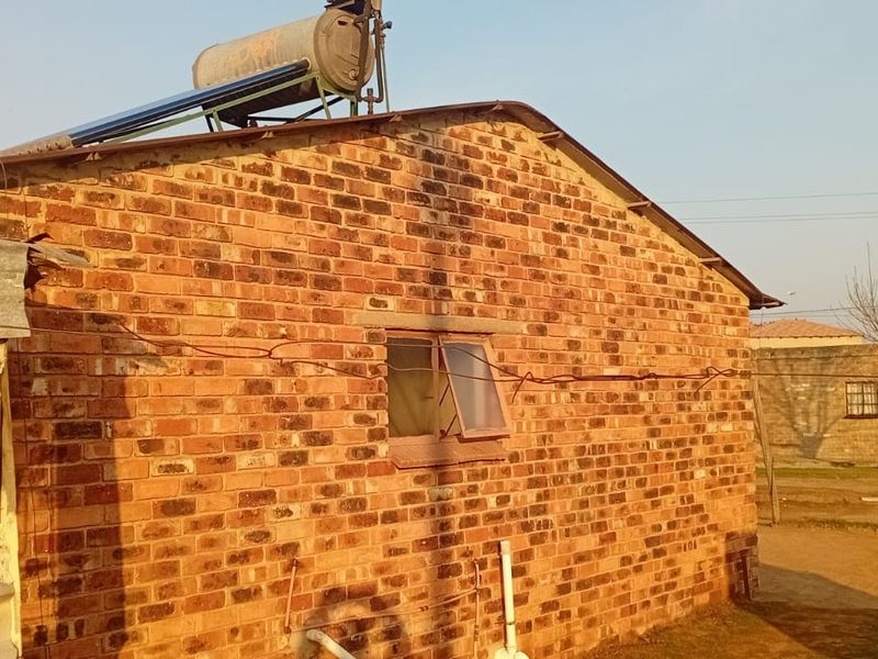 Rear view of a brick house featuring a roof-mounted solar water heater and a metal-framed window.