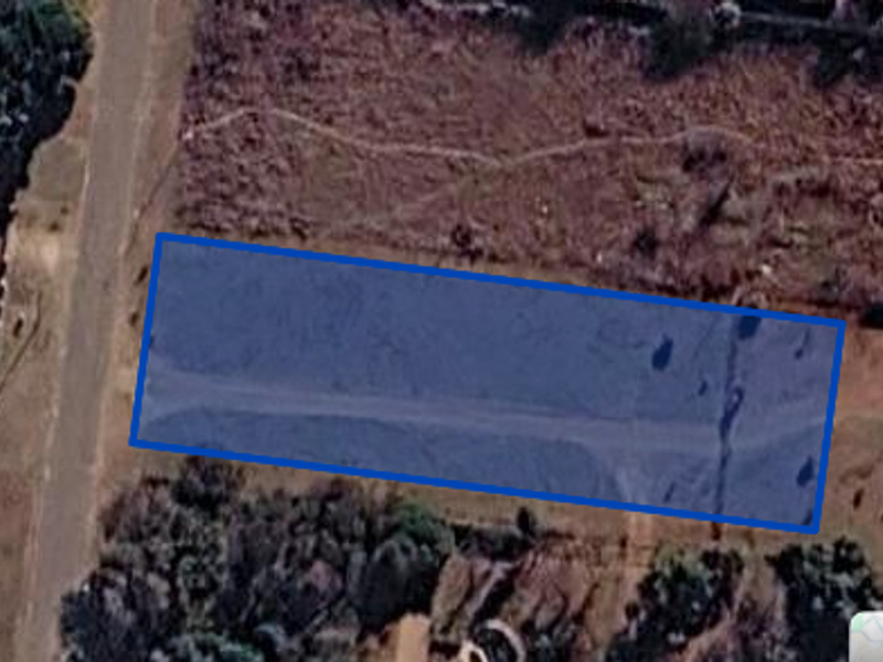 An aerial view showing a rectangular plot of land highlighted in blue, situated within a residential or undeveloped area.
