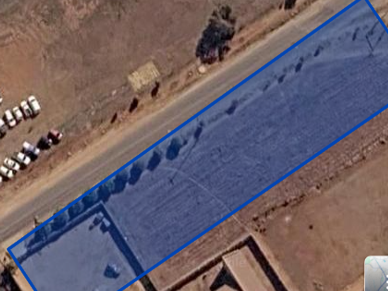 Aerial view of a rectangular plot of land with boundary fencing and paved access, situated adjacent to a public road.